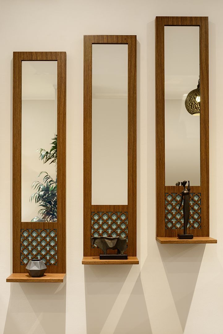 Close-up of three teak jaali mirrors with lattice panels and display shelves against white wall in daylight