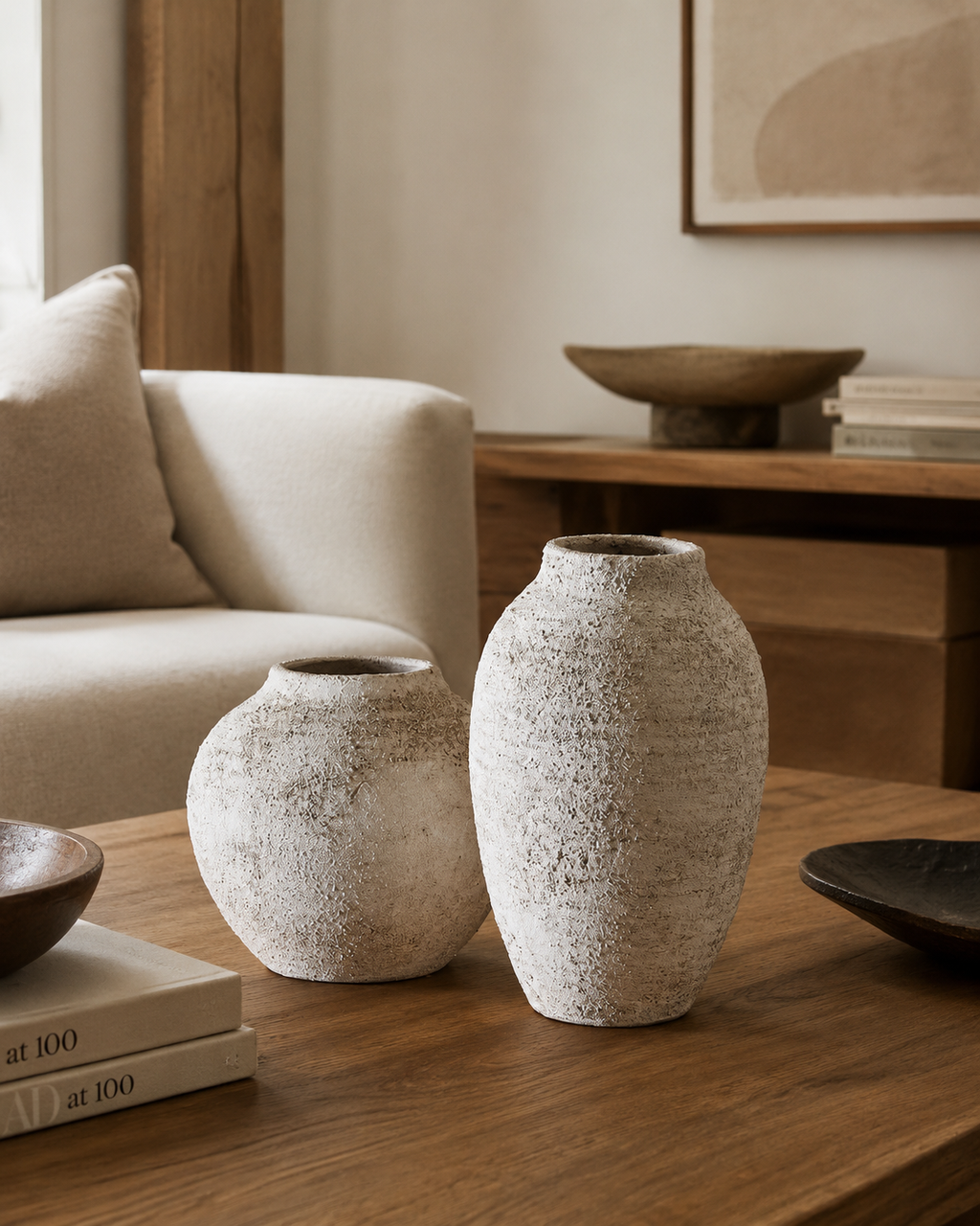 Raw textured stone vase set of 2 on oak coffee table beside cream boucle sofa with art books and wood bowl