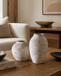 Raw textured stone vase set of 2 on oak coffee table beside cream boucle sofa with art books and wood bowl