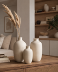 Matte cream ceramic vase trio on oak coffee table with pampas grass beside cream boucle sofa and art books