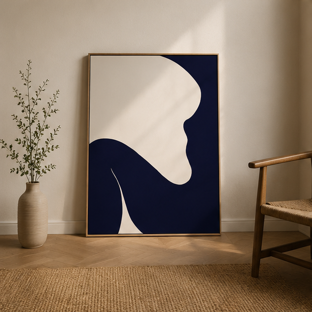 Large navy cream abstract canvas leaning against wall beside rattan chair and ribbed ceramic vase on jute rug