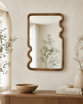 Wavy walnut squiggle mirror above fluted oak sideboard with ceramic vase and Kinfolk books in bright Japandi entryway