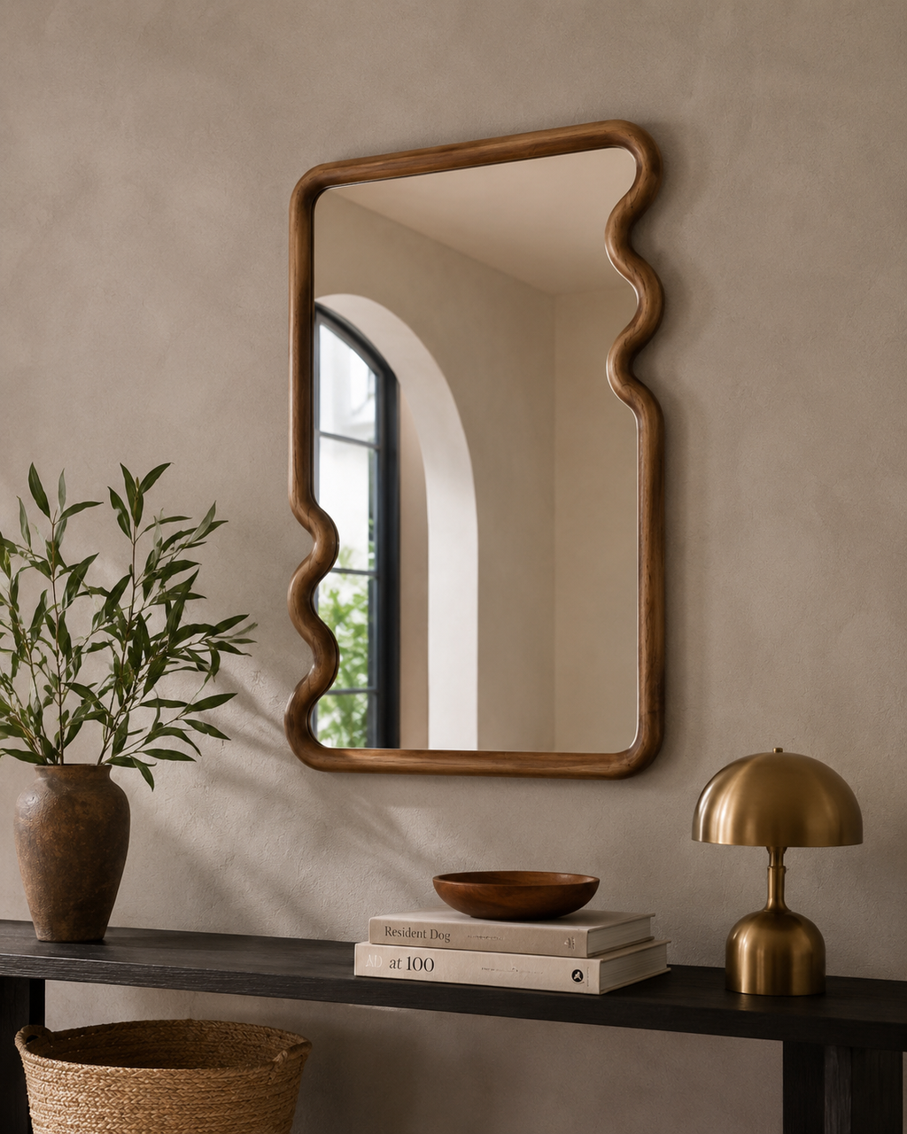 Squiggle walnut mirror above dark console table with brass dome lamp and terracotta vase in warm contemporary entryway
