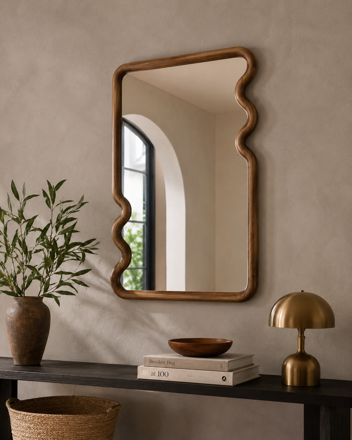 Squiggle walnut mirror above dark console table with brass dome lamp and terracotta vase in warm contemporary entryway